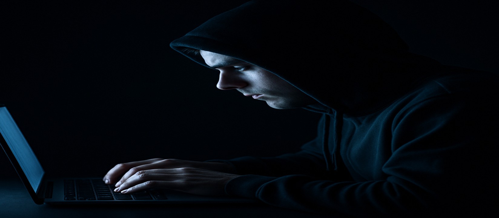 একজন ব্যক্তি অন্ধকার ঘরে ল্যাপটপে মনোযোগসহ 33bt ওয়েবসাইটে অনলাইন গেম খেলছেন